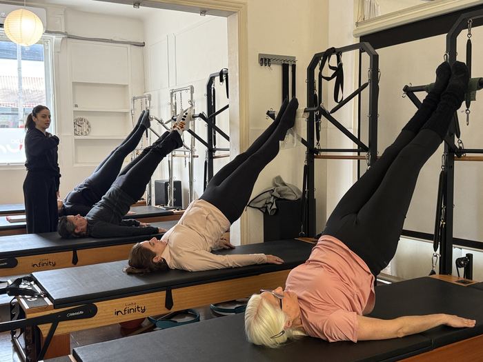 Alumnas trabajando piernas elevadas sobre los Reformers del estudio